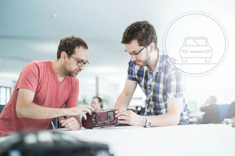 Zwei Mitarbeiter schauen sich ein Modell von einem Auto genau an und besprächen etwas.